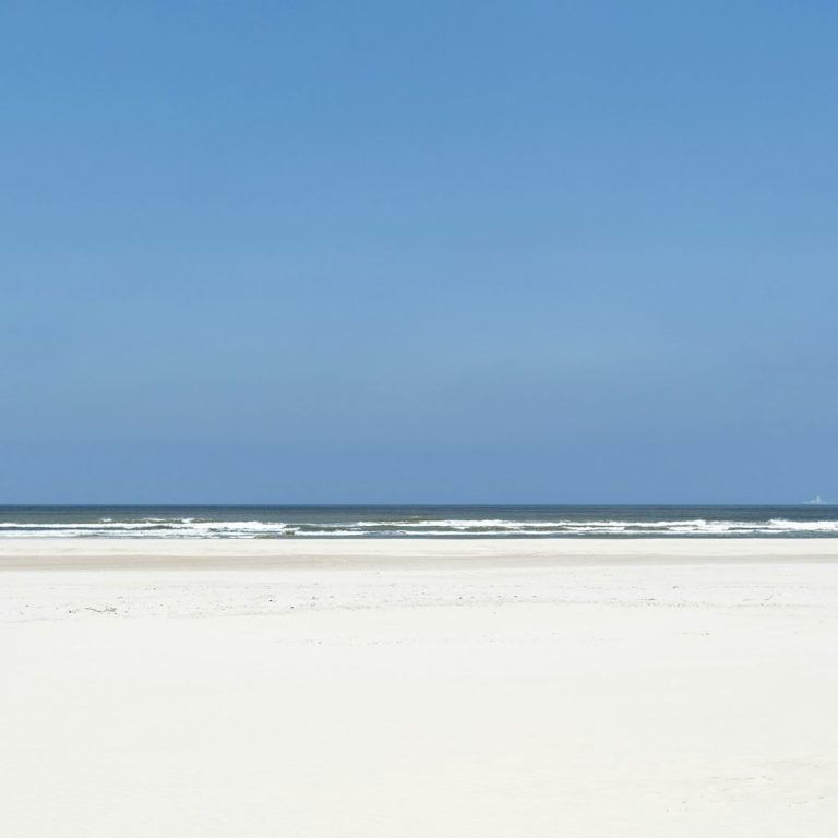 Heller Sandstrand mit sanften Wellen und blauem Himmel.